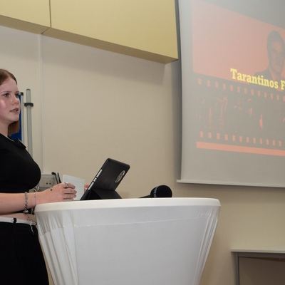 Eine Jugendliche h&auml;lt einen Vortrag mit projizierten Folien auf einer Leinwand.