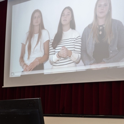 Auf einer Leinwand wird eine Pr&auml;sentation mit drei Jugendlichen gezeigt.
