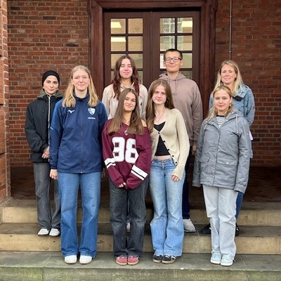 Sch&uuml;lergruppe steht vor einem Backsteingeb&auml;ude auf einer Treppe.