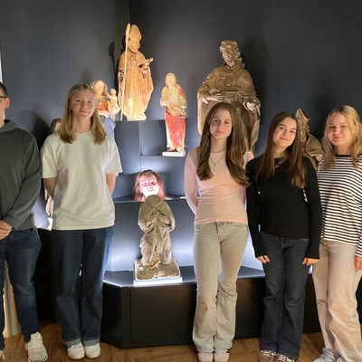 Sch&uuml;lerinnen und Sch&uuml;ler stehen in einem Ausstellungsraum vor historischen Figuren und Objekten.