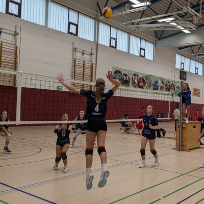 Mehrere Spielerinnen stehen bei einer Volleyballszene am Netz in einer Sporthalle.