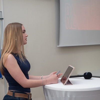 Eine Jugendliche spricht an einem Stehtisch mit Mikrofon.