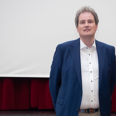 Der Schulleiter steht vor einer Projektionsfl&auml;che in einem Veranstaltungsraum.