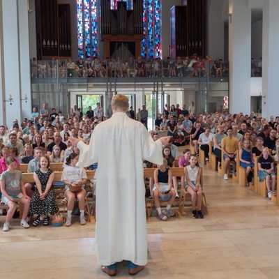 Ein Geistlicher steht vor einer voll besetzten Kirche und spricht zur Gemeinde.