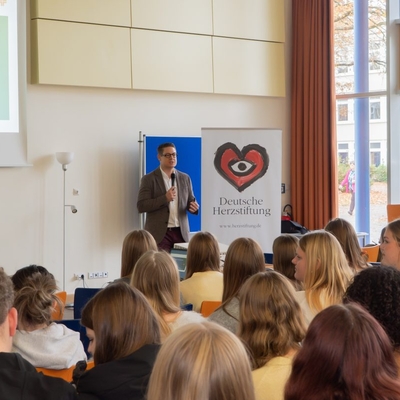 Ein Referent spricht vor sitzendem Publikum in einem Veranstaltungsraum.