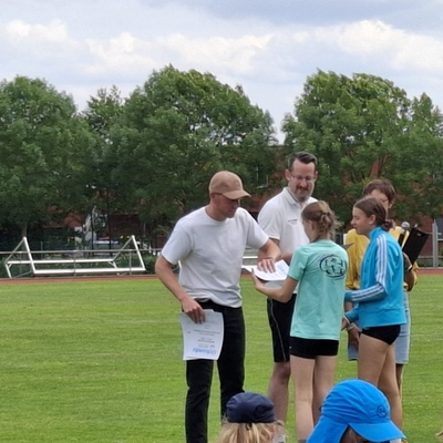 Junge Sportlerinnen bekommen auf einem Sportplatz Urkunden &uuml;berreicht.