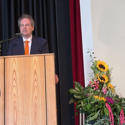 Der Schulleiter h&auml;lt eine Ansprache an einem Rednerpult auf der B&uuml;hne.