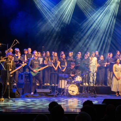 Sch&uuml;lerinnen und Sch&uuml;ler stehen gemeinsam bei einer B&uuml;hnenauff&uuml;hrung im Scheinwerferlicht.