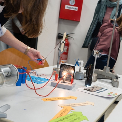 Eine Sch&uuml;lerin probiert an einer Experimentierstation einen Aufbau mit Kabeln und Ger&auml;ten aus.