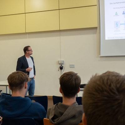 Ein Referent spricht vor sitzendem Publikum in einem Veranstaltungsraum.