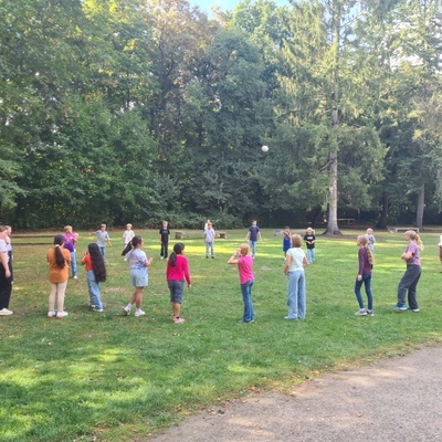 Kinder stehen auf einer Wiese verteilt in einer Reihe bei einem Gruppenspiel.