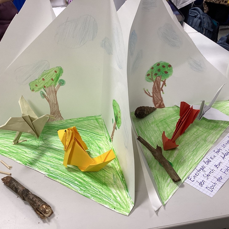 Aufgeschlagene Papierarbeiten mit gebastelten B&auml;umen und kleinen Figuren.