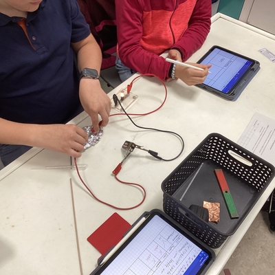 Sch&uuml;lerinnen und Sch&uuml;ler arbeiten mit Messger&auml;ten und Tablets an einem Versuchsaufbau.