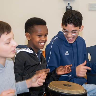 Mehrere Jugendliche trommeln gemeinsam und lachen dabei.