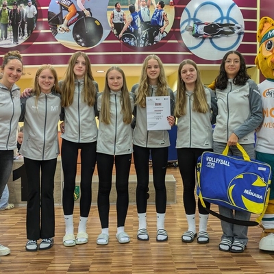Volleyballteam posiert gemeinsam mit einem Maskottchen in einer Halle.